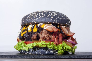 Büyük siyah hamburger, sulu et ve beyaz arka planda yeşillikler.