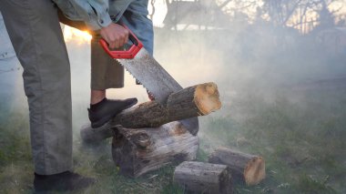 Adam gün batımında duman içinde bir ağaç kesiyor. Siste el testeresi ile tahta testeresi.