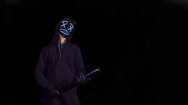 Un uomo con una mazza da baseball con una misteriosa maschera incandescente. Altalene anonime su un nero — Foto Stock