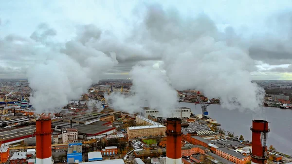 Mavi gökyüzünde, gün batımında şehrin yerleşim bölgesinde dumanı tüten baca manzarası. Termik santralin gri dumanlı üç borusu Telifsiz Stok Fotoğraflar
