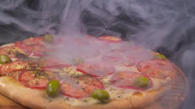 Freshly baked pizza topped with tomatoes, green olives, and herbs, served hot with visible steam rising. High quality 4k footage