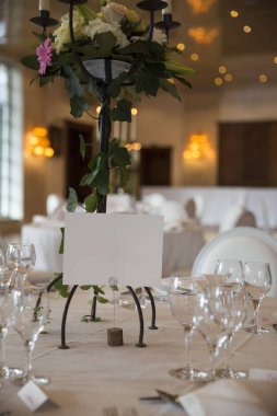 zarif ile servis gözlük, çatal bıçak takımı ve beyaz masa örtüsü ve şamdanlar şık restoran salonu bulanık arka planda yanan mumlar ile çiçek tablolarla dekore edilmiş