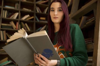 güzel genç kız uzun saçlı bir kütüphanede kitap rafı bulanık bir arka plan üzerinde okuma kitap