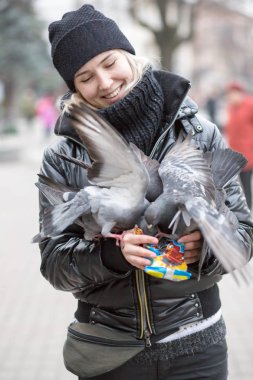 Kuşlar güvercinler Ayçekirdeği bir siyah ceket ve şapka Caddesi'nin arka plan bulanık karşı güzel bir genç kızın elinden yemek.