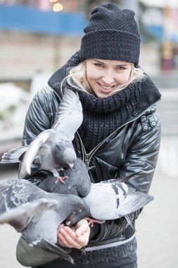 Kuşlar güvercinler Ayçekirdeği bir siyah ceket ve şapka Caddesi'nin arka plan bulanık karşı güzel bir genç kızın elinden yemek.