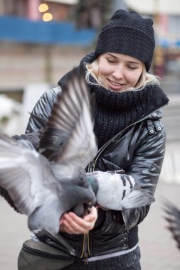 Kuşlar güvercinler Ayçekirdeği bir siyah ceket ve şapka Caddesi'nin arka plan bulanık karşı güzel bir genç kızın elinden yemek.