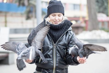 Kuşlar güvercinler Ayçekirdeği bir siyah ceket ve şapka Caddesi'nin arka plan bulanık karşı güzel bir genç kızın elinden yemek.