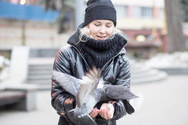Kuşlar güvercinler Ayçekirdeği bir siyah ceket ve şapka Caddesi'nin arka plan bulanık karşı güzel bir genç kızın elinden yemek.