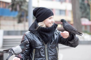 Kuşlar güvercinler Ayçekirdeği bir siyah ceket ve şapka Caddesi'nin arka plan bulanık karşı güzel bir genç kızın elinden yemek.