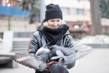 Kuşlar güvercinler Ayçekirdeği bir siyah ceket ve şapka Caddesi'nin arka plan bulanık karşı güzel bir genç kızın elinden yemek.
