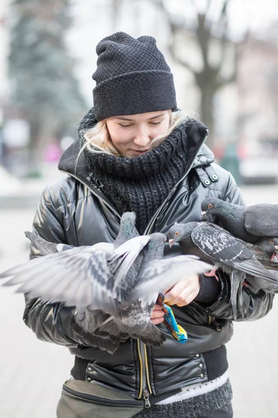 Kuşlar güvercinler Ayçekirdeği bir siyah ceket ve şapka Caddesi'nin arka plan bulanık karşı güzel bir genç kızın elinden yemek.