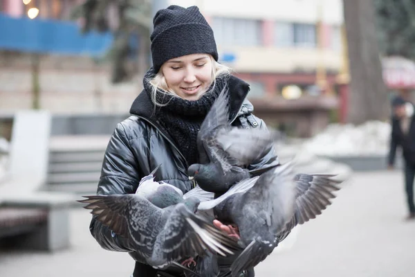 Kuşlar güvercinler Ayçekirdeği bir siyah ceket ve şapka Caddesi'nin arka plan bulanık karşı güzel bir genç kızın elinden yemek.