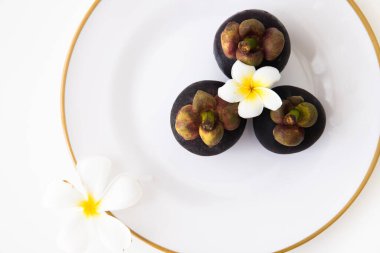 Beyaz arka planda beyaz tesisat çiçekleri olan beyaz bir tabakta üç tane Tayland mangosteen meyvesi..