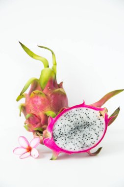 Beyaz bir zemin üzerinde pembe bir plumeria çiçeğiyle birlikte bir buçuk ejderha meyvesi..