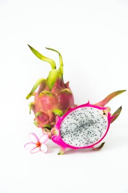 Beyaz bir zemin üzerinde pembe bir plumeria çiçeğiyle birlikte bir buçuk ejderha meyvesi..
