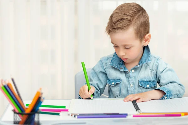 Petit garçon qui fait des devoirs d'écriture et de peinture. Le préscolaire apprend à écrire et à dessiner . — Photo