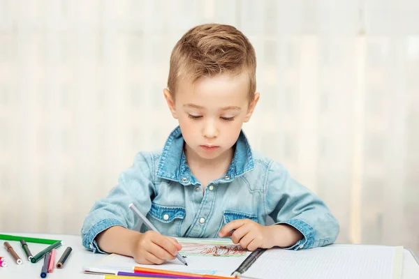 Cute boy doing homework writing and painting. Children paint