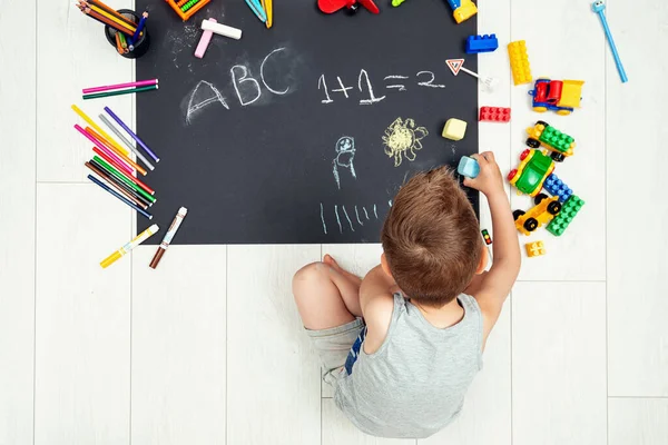 Adorable niño sentado solo usando tiza pintura sobre papel negro — Foto de Stock