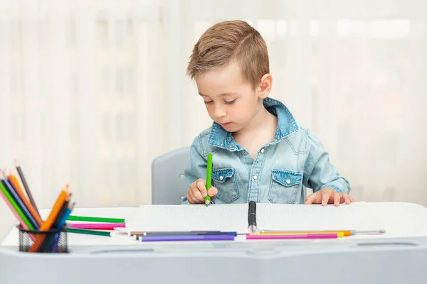 Un niño haciendo deberes escribiendo y pintando. Preescolar aprender a escribir y dibujar . —  Fotos de Stock