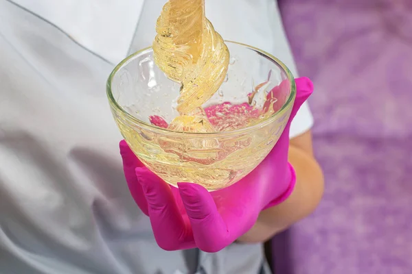 Master of depilation in pink latex gloves pulls out a wooden stick sugar paste from the bowl