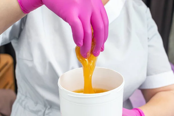 Close up golden liquid sugar into a white jar in the hands of a depilation master