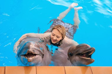 Yunus terapisi seansı. Genç kız gülümsüyor ve iki yunusa sarılıyor.