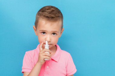 Mavi arka planda anti-alerjik burun spreyi olan bir çocuğun portresi.
