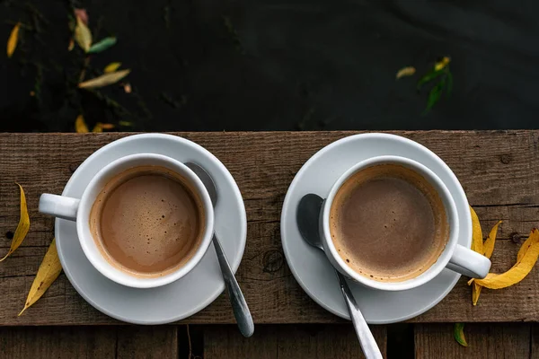 Dwie białe filiżanki kawy z mlekiem na drewnianej podłodze nad rzeką — Zdjęcie stockowe