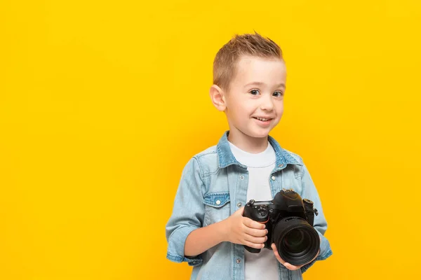 Feliz niño sostiene la cámara fotográfica profesional, sonríe y mira a la cámara —  Fotos de Stock