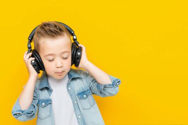 Mavi kot gömlekli komik çocuk kulaklıkla müzik dinliyor ve eğleniyor.