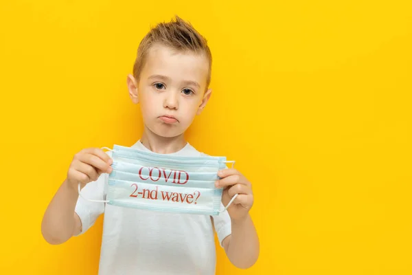 Triste niño sosteniendo una máscara médica con la inscripción con una pregunta Covid segunda ola —  Fotos de Stock