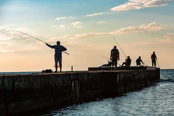 Des pêcheurs masculins silhouettés. Pêcheurs avec cannes à pêche jettent l'appât dans l'eau sur la jetée de la mer — Photo