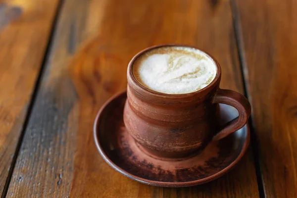 Kawa z mlekiem lub cappuccino w brązowym glinianym kubku na drewnianym stole. — Zdjęcie stockowe