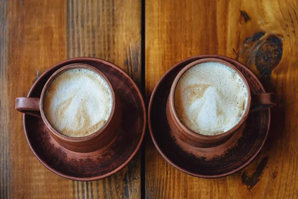 Dwie retro filiżanki kawy. Latte w ciemnobrązowych glinianych kubkach na drewnianym stole. — Zdjęcie stockowe