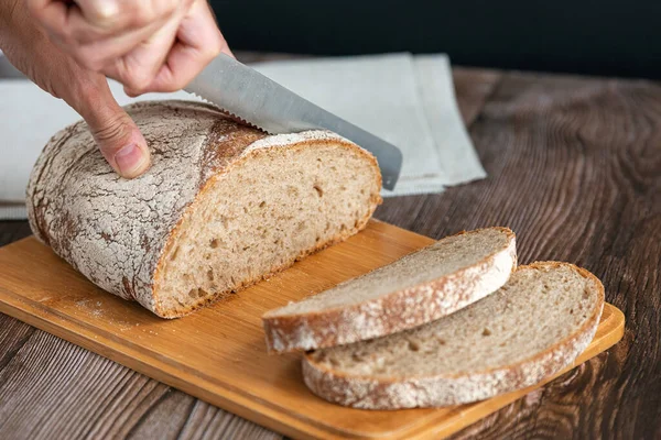 Close up of hands cutting a slice of bread. Male hands cutting bread on wooden board