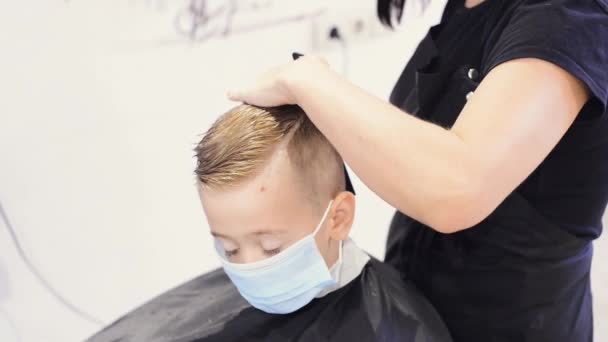 Coiffure pendant la pandémie de COVID-19. Client enfant en masque de protection pendant la coupe de cheveux — Video