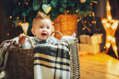 Noel süslemelerine karşı sepette yerde duran sevimli bir çocuk. Tatil sezonu. Yeni yıl tatili. 