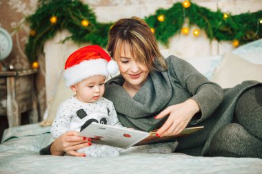 Anne ve oğlu yatakta oturup birlikte yılbaşı masalları okuyorlar. Noel süslemeleriyle birlikte aile portresi..