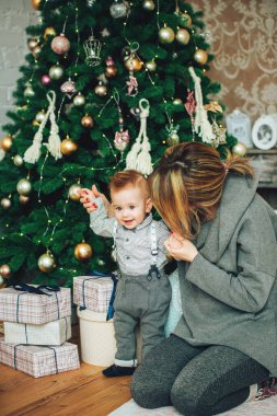 Genç anne Noel süslemeli ağaç ve hediye kutularının yanında oğluyla oynuyor. Noel mucizeleri. Mutlu yıllar.