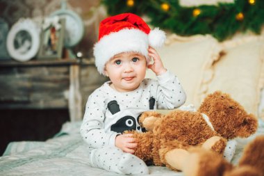 Kırmızı Noel şapkası takan küçük çocuk komik bir şekilde dilini gösteriyor. Neşeli bir beyaz, bir yaşında bir çocuk. Mutlu yıllar.