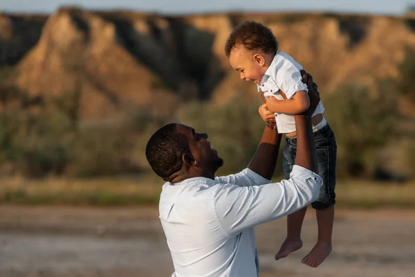 Happy African American father and son having a good time outdoors. Father having fun throws up in the air his child. Happy father\'s day concept.