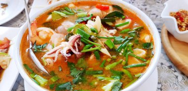 Sıcak deniz ürünleri çorbasını sebzeli, kaşığı da yemek masasında beyaz kâse ile birlikte restoranda öğle yemeği için kapayın. Tayland Tom Yum ve Tayland 'da meşhur yemekler.