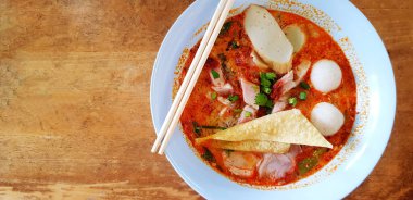 Çorba, yemek çubuğu, bol yağda kızartılmış ton et, balık ya da tavuk topu, gevrek domuz eti ve ahşap masada ya da arka planda sol fotokopi alanı olan açık mavi bir kasede. Asya yemekleri