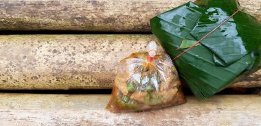 Plastik torba dolusu baharatlı tavuk, fesleğen ve pirinç ile karıştırılmış muz yaprakları yerine sol fotokopi alanı ile kahverengi kuru bambu masasında servis yapın. Öğle yemeği, doğal malzeme ve doğa rezervi.