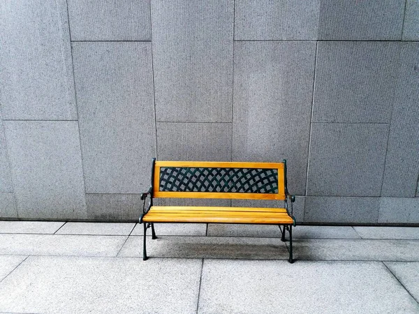 Yellow bench on white or gray concrete wall background with copy space on above - available seat, alone and relaxing