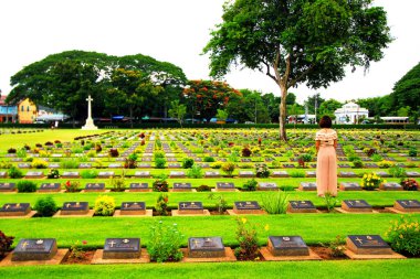 Kanchanaburi, Thailand - April 12, 2023: Asian woman standing in front of black gravestone at graveyard. Reminisce, miss, sad and lose person in the family or important people concept.