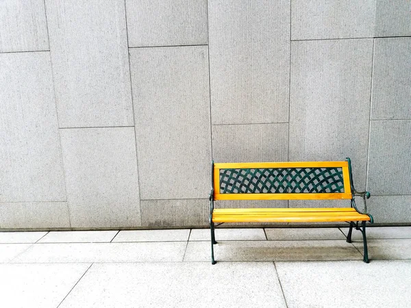 Yellow bench on white or gray concrete wall background with copy space - available seat, alone and relaxing