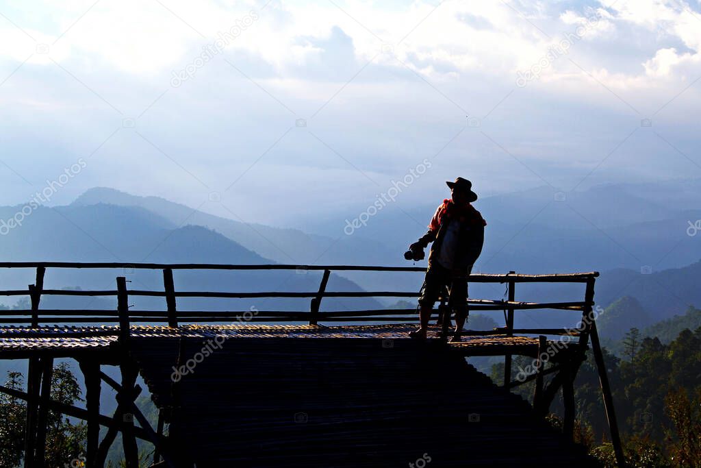 Silhouette of Tourist man standing and holding camera with mountain and blue sky background at view point of Doi Ang Khang, Chiangmai, Thailand.