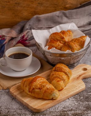Kahvaltı için gri masadaki koyu kahveyle taze pişmiş kruvasanlar.