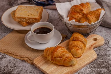 Taze pişmiş kruvasan ve kahvaltı için gri masada sade kahve ile tam buğday ekmeği.